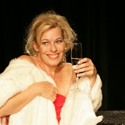 Gabriele Misch im weißen Pelz mit Sektglas, lachend